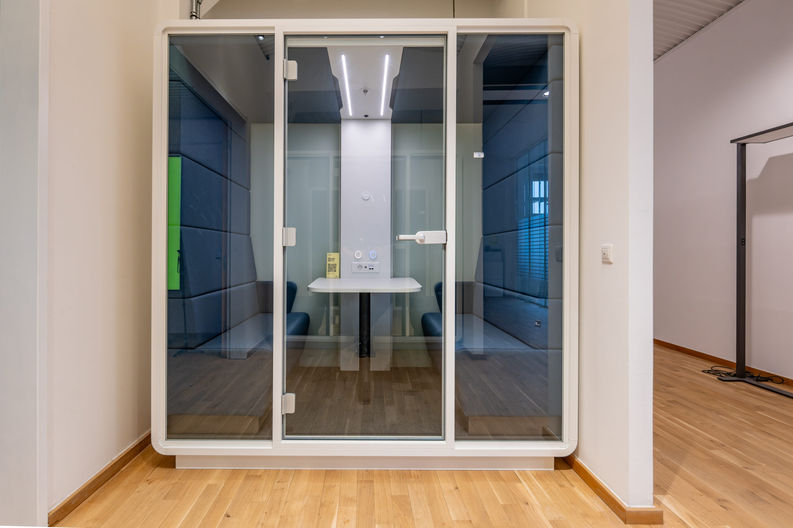 A white glass-walled acoustic meeting pod in an office.