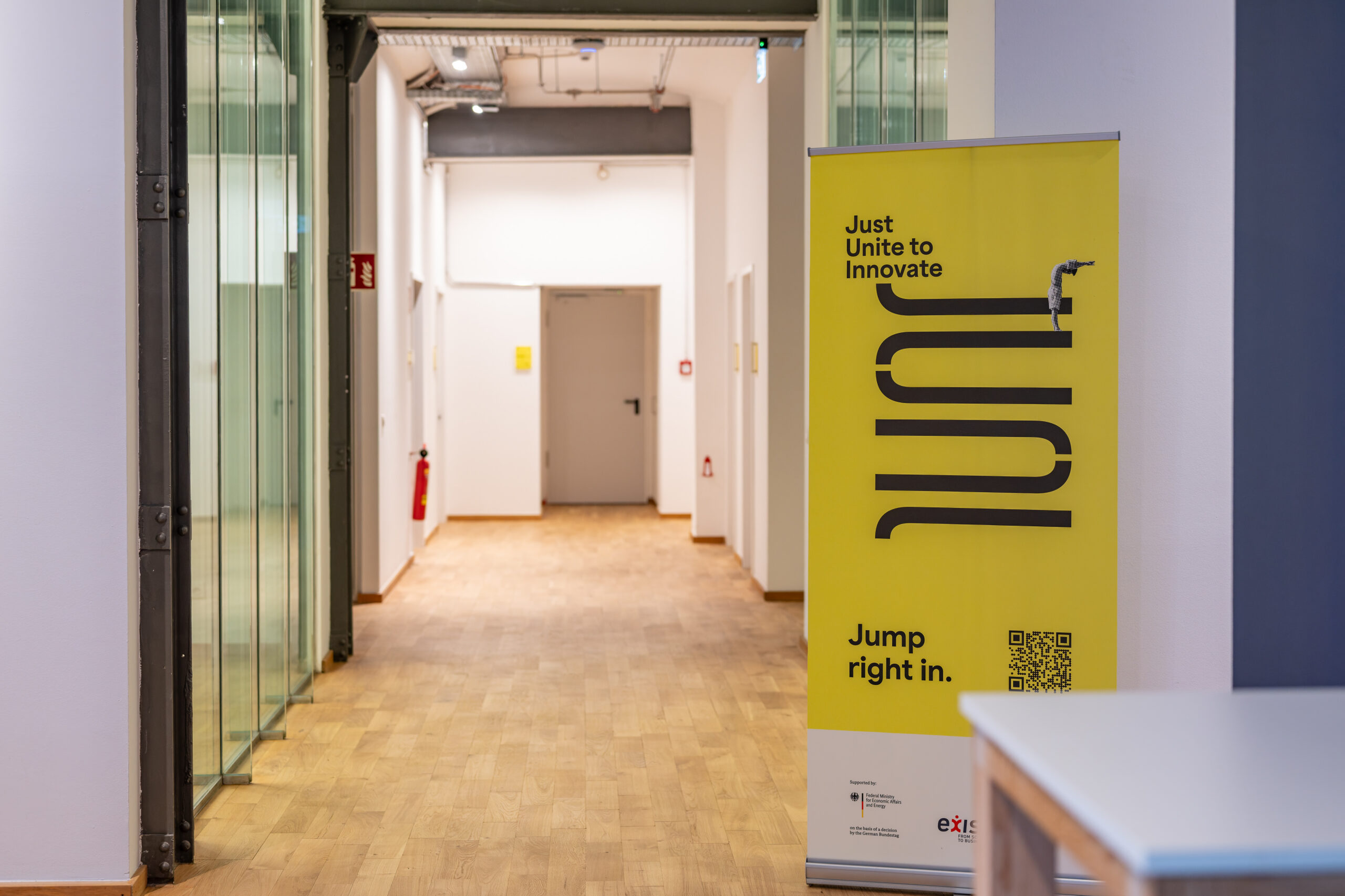 Yellow JUNI banner standing in a modern office hallway.